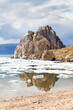 Baikal Lake on Spring. View of natural landmark of Olkhon Island - Shamanka Rock during ice drift on sunny May day. Sandy beach with reflection of rock near Khuzhir village. Scenic spring landscape