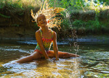 Fototapeta Lawenda -  little girl playing in the river. A girl with blond hair in a sunbeam surrounded by thousands of small drops.
