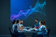 © master1305 - Teammates in a corporate environment sit around a conference table, focusing on a digital stock chart displayed on a monitor in the boardroom. Concept of business, trade market, economics, finances