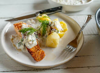 Wall Mural - Pan fried salmon fillet with light yogurt apple dill sauce and boiled potatoes on a plate on kitchen table