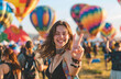 Portrait of an excited woman making the rock and roll sign with her fingers up, standing in front of a colorful hot air balloon festival