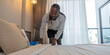 Young African American man clean making bed. happy black man changing bedsheets at home standing in bedroom