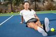 © Mat Hayward - Young female pickleball player sitting outside on the court. She is holding paddle or racquet and surrounded by yellow game balls.