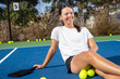 © Mat Hayward - Young female pickleball player sitting outside on the court. She is holding paddle or racquet and surrounded by yellow game balls.