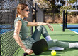 © Mat Hayward - Female pickleball player wearing a green body suit sits on the court between games. The woman is wearing sunglasses and is sitting comfortably with a paddle and a ball.