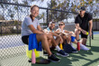 © Mat Hayward - Group of four friends sitting together on a pickleball court after a fun game. The diverse people include African American or black, Asian, and Caucasian or white.