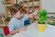 Boy watering a plant from a toy watering can in a kindergarten