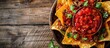 Nachos made with Mexican corn tortilla chips topped with seasoned meat and spicy red salsa, pictured on a wooden background with copy space.