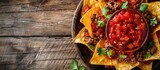 Fototapeta  - Nachos made with Mexican corn tortilla chips topped with seasoned meat and spicy red salsa, pictured on a wooden background with copy space.