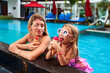 Mother, daughter enjoy ice cream by resort pool. Little girl in swim goggles eats dessert with mom on sunny day. Happy family moments, luxury vacation lifestyle. Child, parent share treat outdoors.