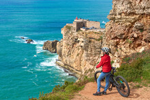 Nice Senior Woman Riding Her Electric Mountain Bike On The Rocky Cliffs Of Nazare At The Western Atlantic Coast Of Portugal