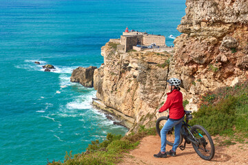 Wall Mural - nice senior woman riding her electric mountain bike on the rocky cliffs of Nazare at the western atlantic coast of Portugal