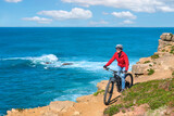 Fototapeta Natura - Brave senior woman riding her electric mountain bike on the rocky cliffs of Peniche at the western atlantic coast of Portugal