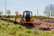 Excavator digging trench in soil for pipeline during building house. Machinery for construction. Piping by foundation