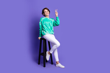 Poster - Full size photo of attractive young woman sit chair show v-sign dressed stylish green clothes isolated on violet color background