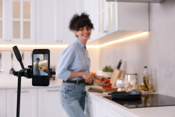 Wall Mural - Food blogger cooking while recording video in kitchen, focus on smartphone