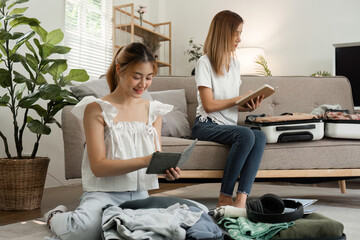 Two young female friends pack a suitcase with clothes and travel passports in preparation for a weekend away.