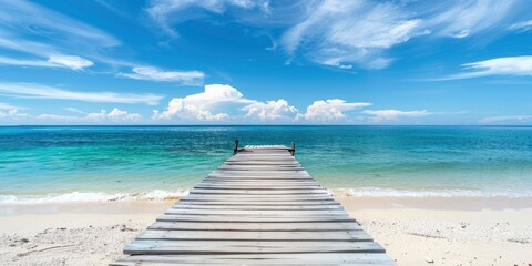 Wall Mural - A white sand beach with a blue sky has a wooden pier that leads to the ocean.