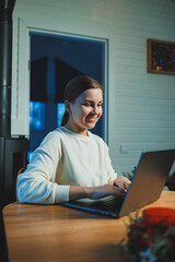 Wall Mural - Smiling happy woman working on laptop while sitting at table. Young creative woman working and typing on keyboard at home. Work at home concept