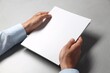 © New Africa - Man holding blank notebook at light grey table, closeup. Mockup for design