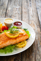 Sticker - Fried salmon steak, French fries and fresh vegetable salad served on wooden table
