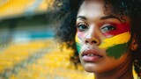 Fototapeta Kosmos - beautiful woman with face painted with the flag of Cameroon in a stadium. Olympic games concept, world sporting event in high resolution