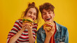 A joyful pair of friends, a girl in a striped shirt and a boy in a denim jacket, giggling as they pose with their cheeseburgers in hand.