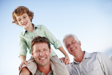 Canvas Print - Portrait of grandfather, father and child by blue sky for bonding, relationship and relax together. Family, generations and grandpa, dad and young boy on shoulders for holiday, vacation and weekend