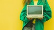 Crop unrecognizable woman in green outfit holding computer on green background