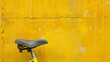 Yellow bike seat and part of wheel with a yellow wall in the background.