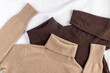 Soft sweaters of beige and of brown luxury natural cashmere lying on white linen background.  Autumn and winter  pure wool clothing