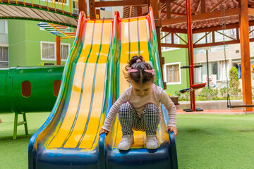 Una linda niña de dos años sonriente juega en un tobogan dentro del patio de un condominio.