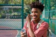 © Jovo Jovanovic/Stocksy - Happy teenage student enjoying music through phone at sports court