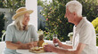 © peopleimages.com - Senior, couple or pineapple on patio with water for retirement, planning vacation for anniversary. Husband, wife or old in garden for talk with drink, sunshine in summer with partner in home for chat