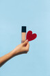 © Ángela Rober/Stocksy - Woman's hand holding a decorative red heart and make-up base