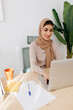 © Tania Cervian/Stocksy - Cheerful woman in hijab working at table with computer