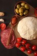 Pizza dough and products on dark table, flat lay