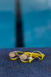 Yellow swimming goggles resting on blue poolside indoors, no people visible, copy space