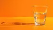 Clear glass half full of water on orange background with reflection and shadow