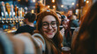 An enthusiastic woman taking a selfie with a group of friends at a beer festival, with taps and patrons softly out of focus behind her. Shallow depth of field, blurred background