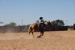 Western rodeo industry concept with young child cowboy riding palomino horse through outdoor arena for roping practice.