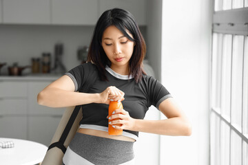 Poster - Sporty Asian woman with bottle of juice in kitchen