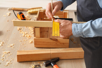 Wall Mural - Mature carpenter measuring wooden box at table in workshop, closeup