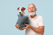 Senior man with cute dog in basket on light blue background