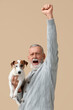 Happy senior man with cute dog on beige background