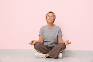 Sticker - Portrait of meditating mature woman sitting on floor against pink wall