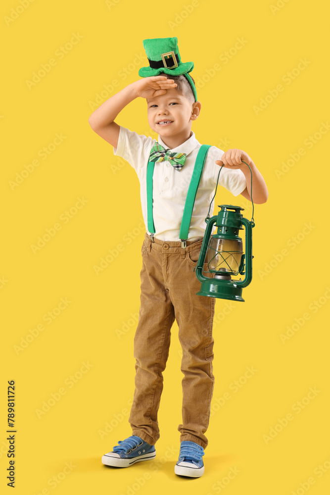 Cute little boy with leprechaun's hat and lantern on yellow background. St. Patrick's Day celebration