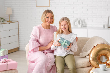 Wall Mural - Beautiful young woman and her cute little daughter with gift box sitting on sofa in living room