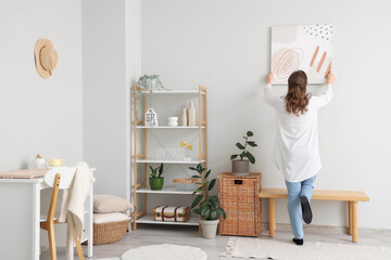 Wall Mural - Young woman hanging picture on white wall in room