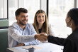 © fizkes - Cheerful young couple shaking hands with African American lawyer, broker, consultant, real estate agent, thanking for consultation. Positive business partners giving handshake at meeting, smiling